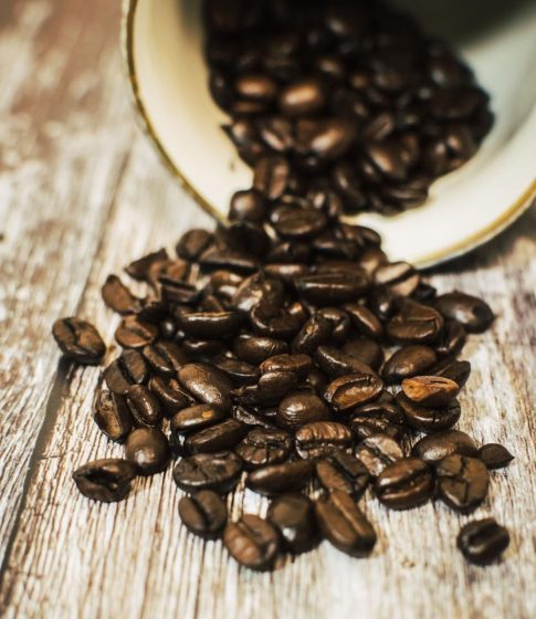 close up view of dark roasted coffee beans spilling from a mug